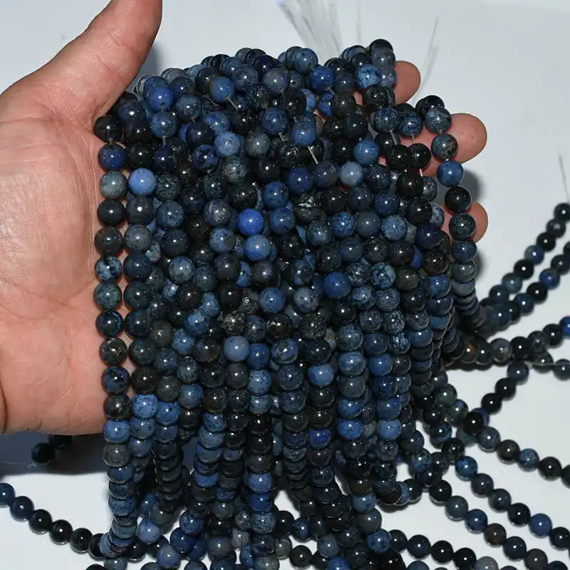 Dumortierite Beads Wholesale strands displayed by hand for size reference