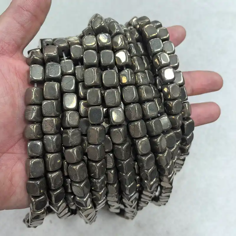 8x10mm Pyrite Beads Wholesale – multiple metallic gray bead strands draped across an open hand