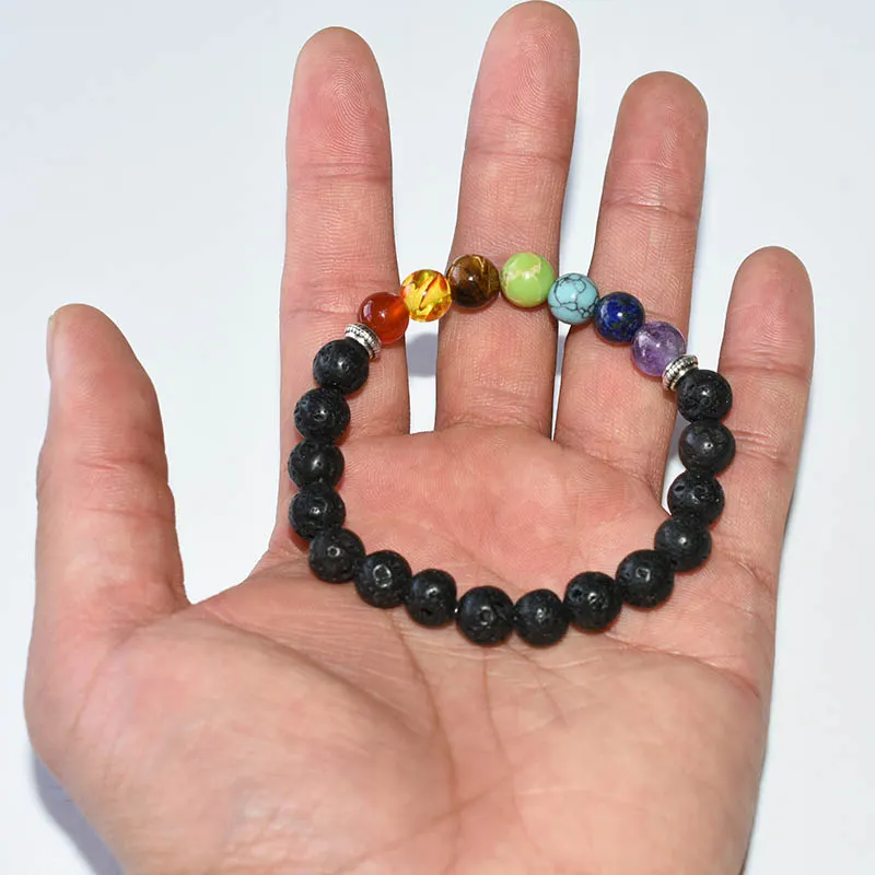 Chakra Bracelets Wholesale showing a black lava bead bracelet with seven colored beads on an open palm